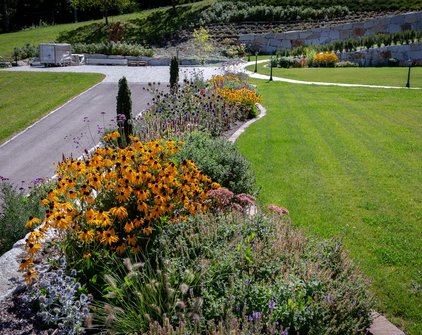 Farbenfrohes Staudenbeet mit Sonnenhut (Rudbeckia) entlang eines Gartenwegs vor einer terrassierten Hanggestaltung mit Naturstein.